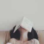 A woman relaxes indoors with an open book resting on her face, enjoying a tranquil moment.