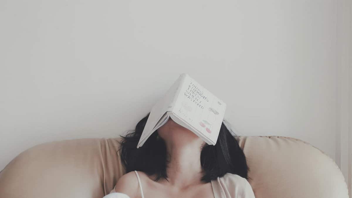 A woman relaxes indoors with an open book resting on her face, enjoying a tranquil moment.