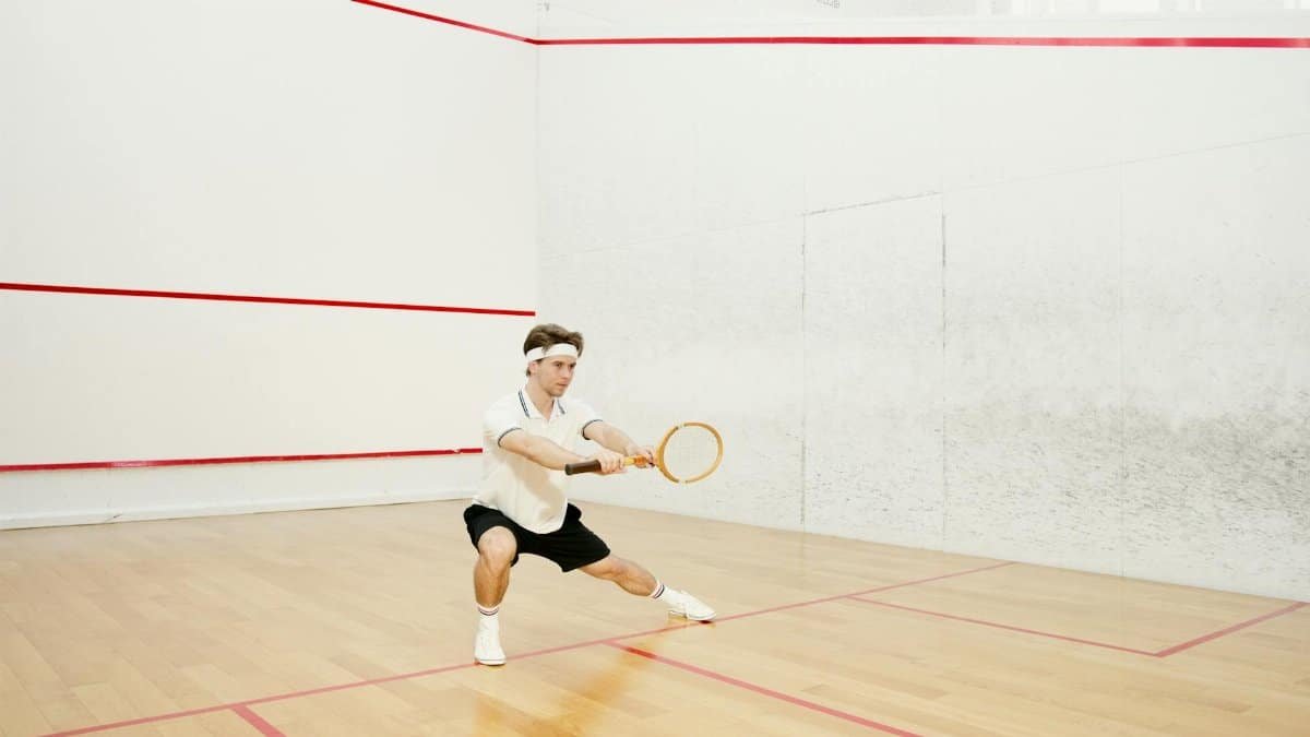 Focused male athlete stretching and holding racket on indoor squash court.