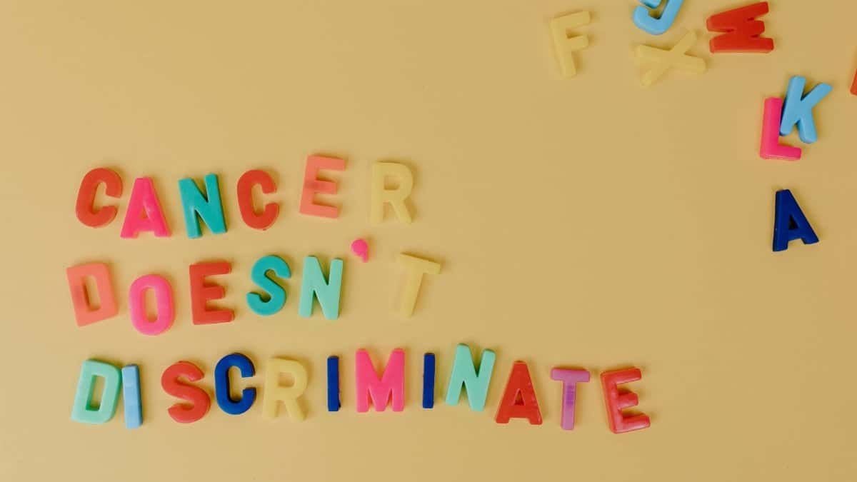 Vibrant letters spell out 'Cancer Doesn't Discriminate' on a yellow background, promoting cancer awareness.