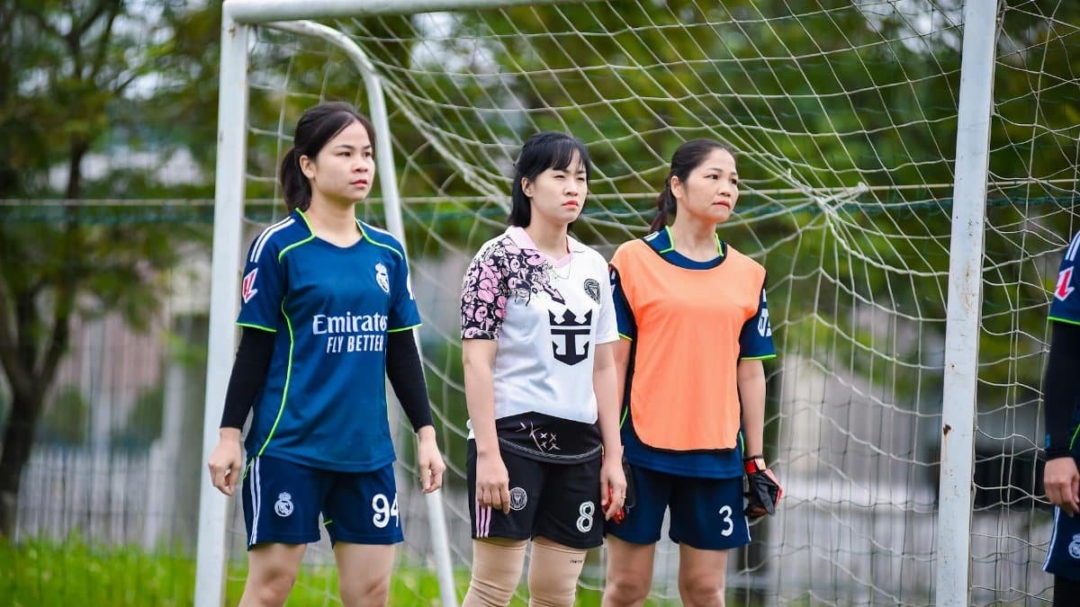 Three female football players stand by the goal post, showcasing team spirit in Hanoi, Vietnam.