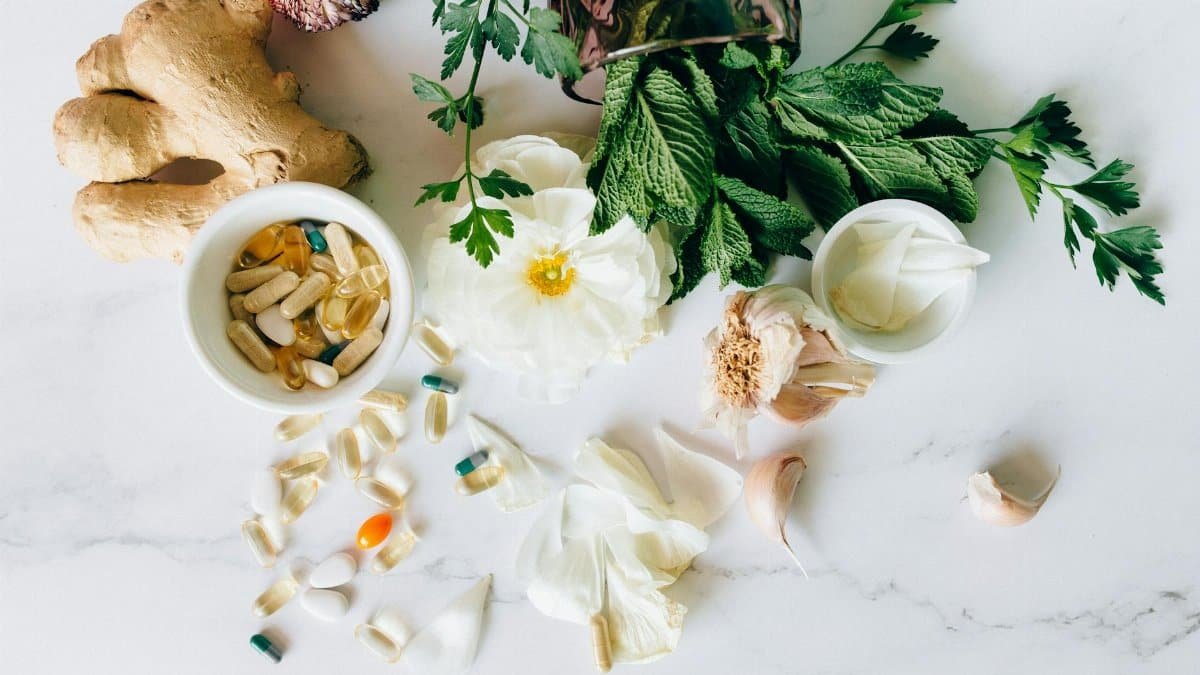 A flatlay of herbal supplements with fresh ginger, garlic, and leaves.