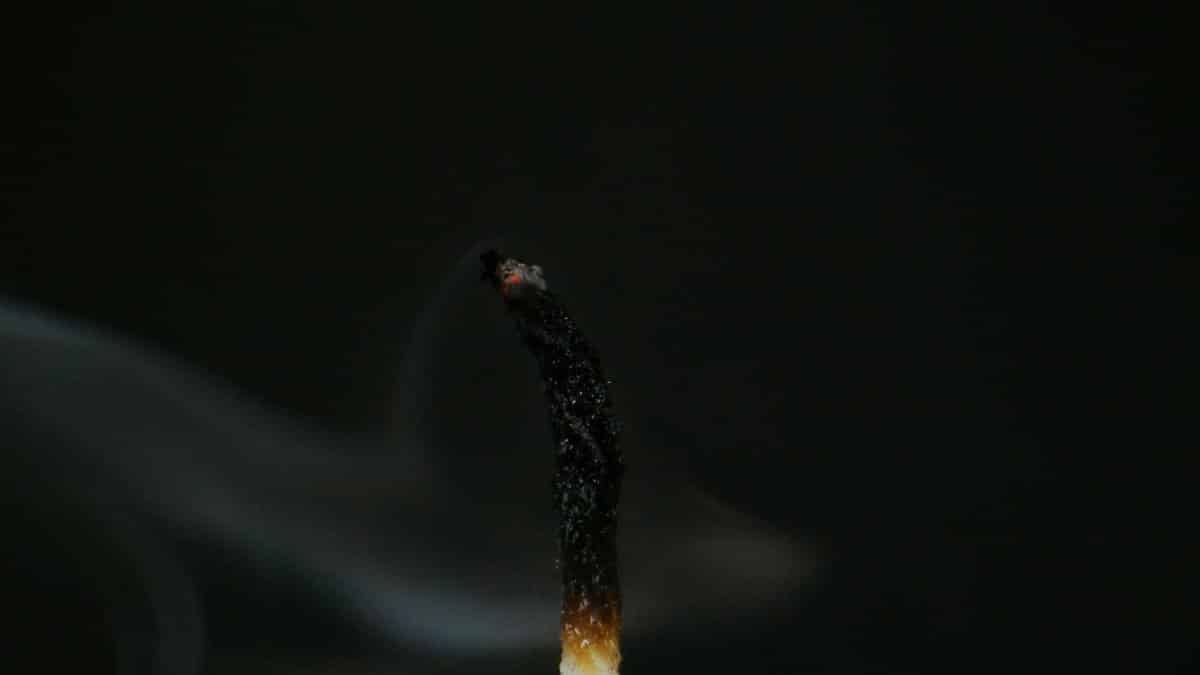 Detailed view of a burnt matchstick with rising smoke against a dark background.