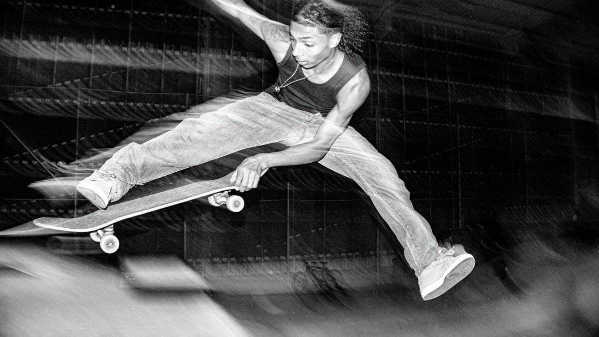 A skateboarder performs an aerial trick indoors in a high-energy black and white photo.