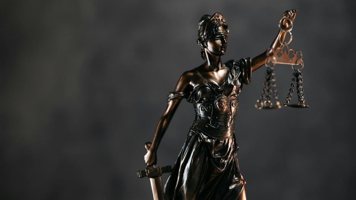 Detailed bronze Lady Justice statue with scales and sword against a dark background, symbolizing law and justice.