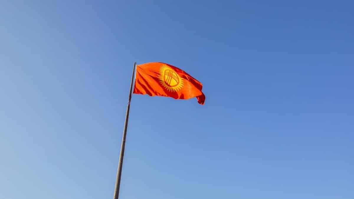 Red national flag of Kyrgyzstan waving on a flagpole under a clear blue sky.