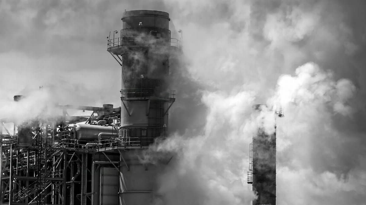 Black and white photo of smokestacks in an industrial area emitting thick smoke, highlighting pollution.