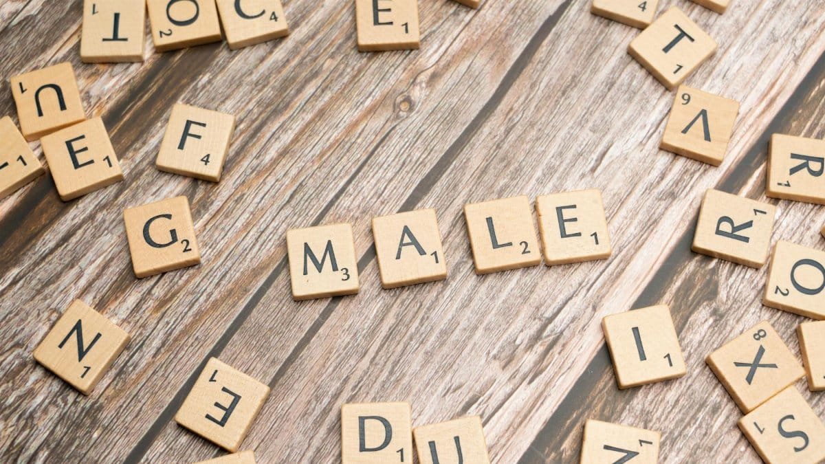 Close-up of wooden letter tiles forming the word 'Male' on a wooden surface with scattered tiles.