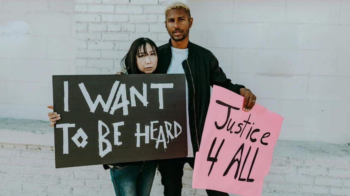 Two individuals holding protest signs advocating for equality and justice against a brick wall.