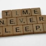 Wooden Scrabble tiles arranged to spell 'Time Never Sleeps' on a white background.