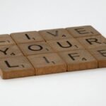 Wooden Scrabble tiles spell out 'Live Your Life' on a white surface. Encouraging and minimalist.