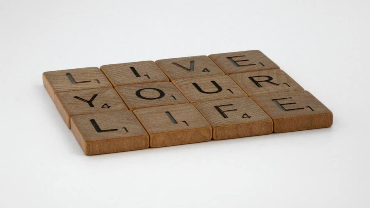 Wooden Scrabble tiles spell out 'Live Your Life' on a white surface. Encouraging and minimalist.