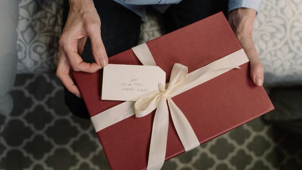 Close-up of hands holding a red gift box with a white ribbon and a message tag.