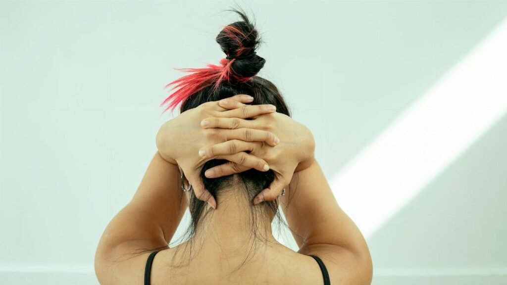 A woman performing yoga indoors, hands clasped behind head, stretching gracefully.