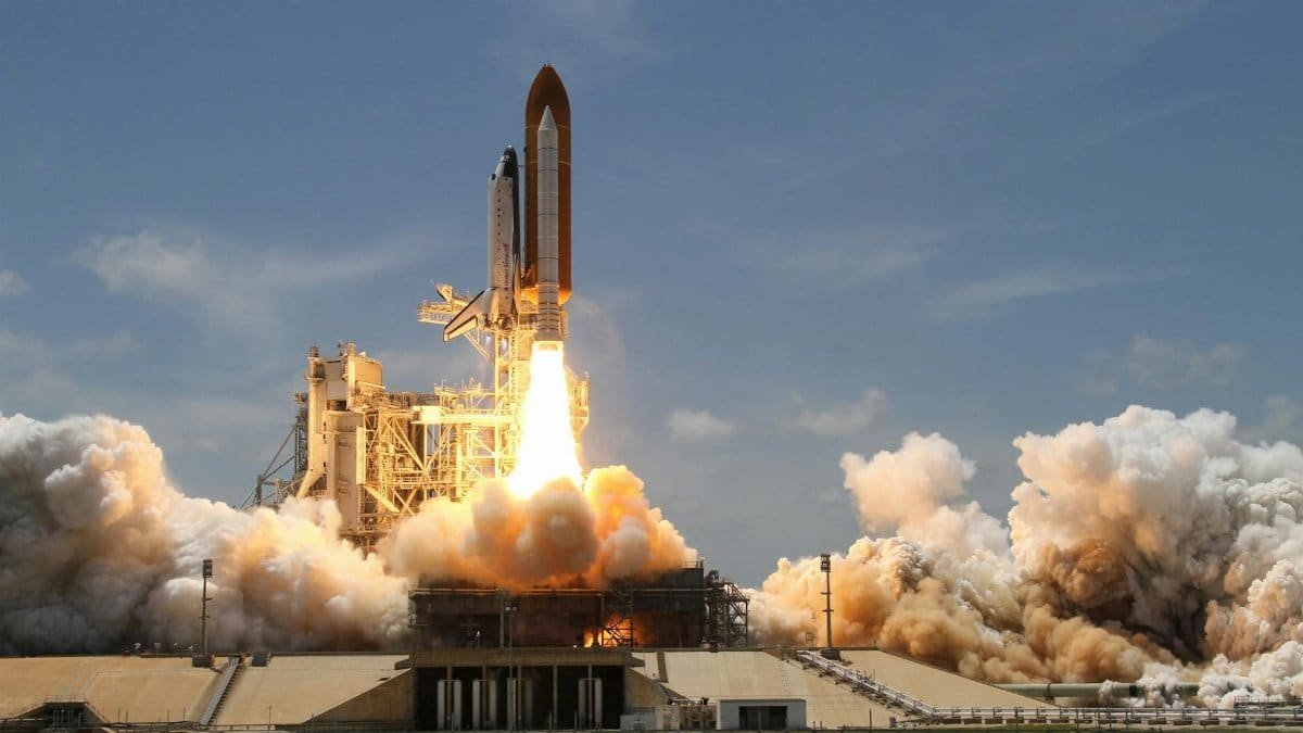 A NASA space shuttle launches with fiery liftoff, ascending into the sky amid plumes of smoke.