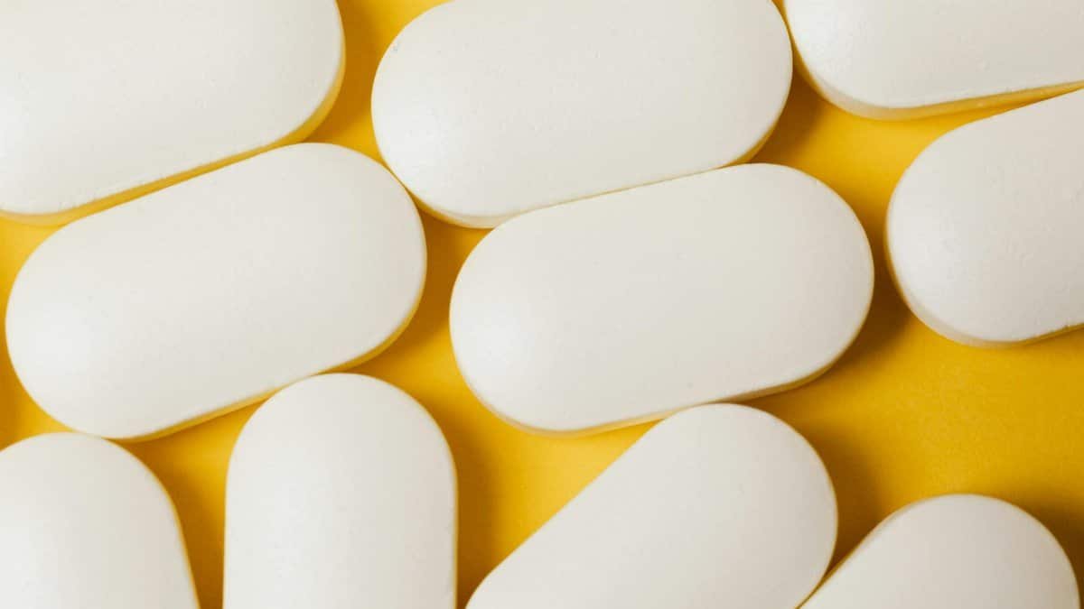 From above closeup of white ellipse shaped medical pills placed on bright yellow surface