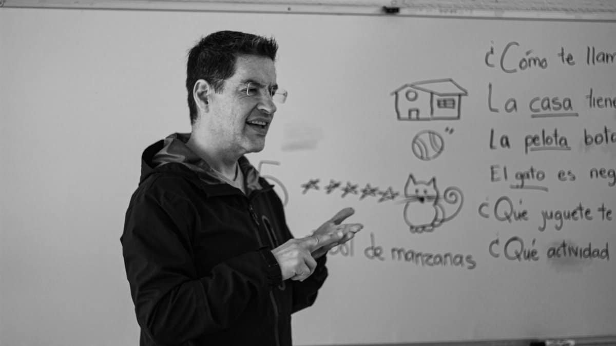 A Spanish teacher explaining language concepts on a whiteboard in class.