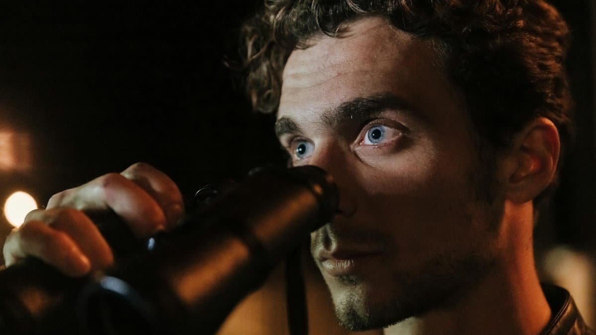 Close-up of a man with intense gaze using binoculars during night time observation.