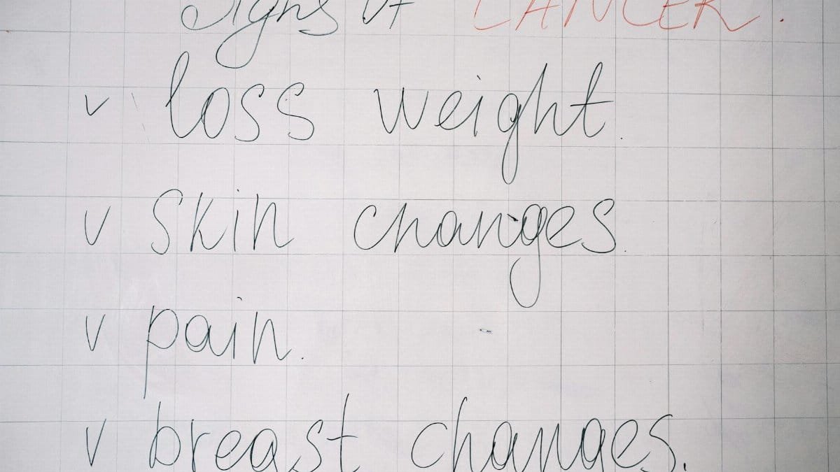 List of cancer symptoms handwritten on a whiteboard including weight loss and skin changes.