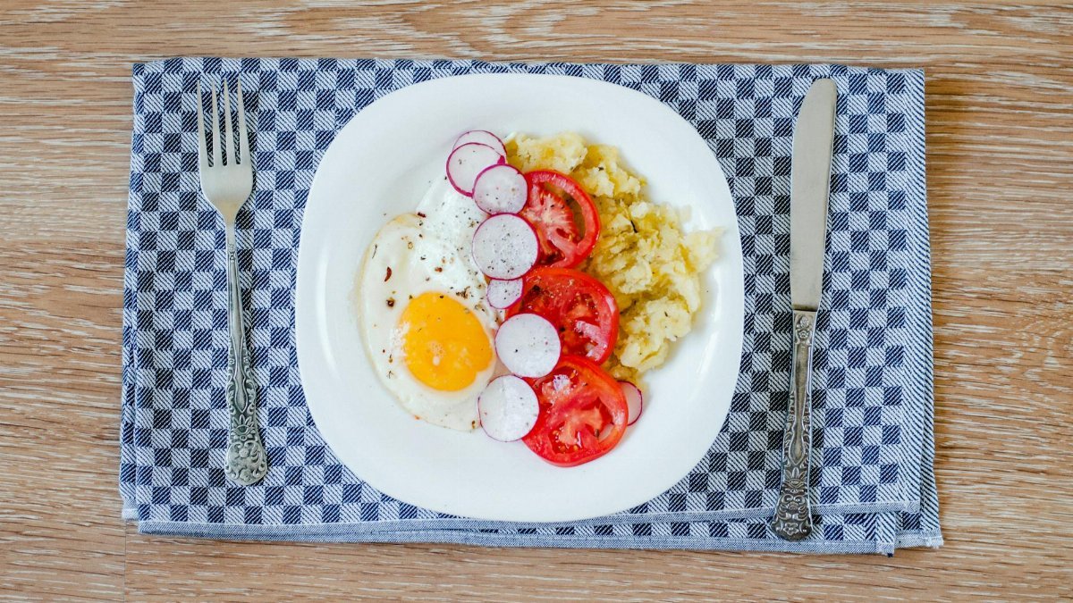 A delicious breakfast featuring fried eggs, tomatoes, radishes, and smashed potatoes.