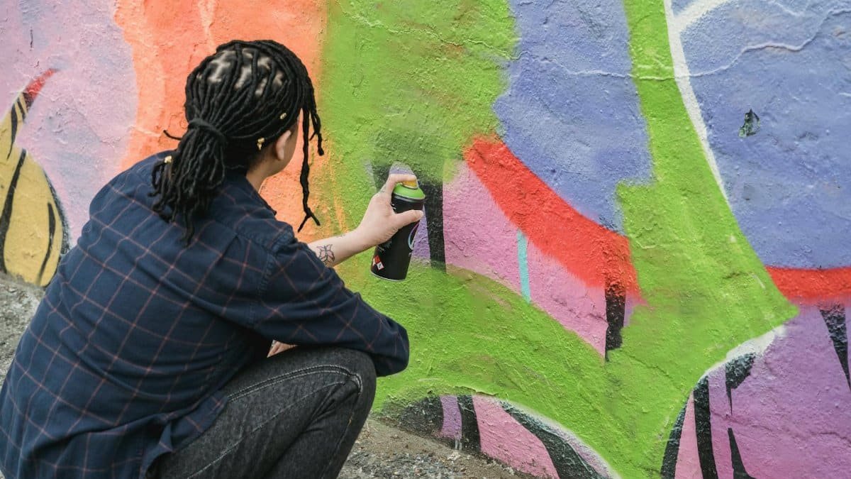 Artist spray painting vibrant graffiti on a wall outdoors.