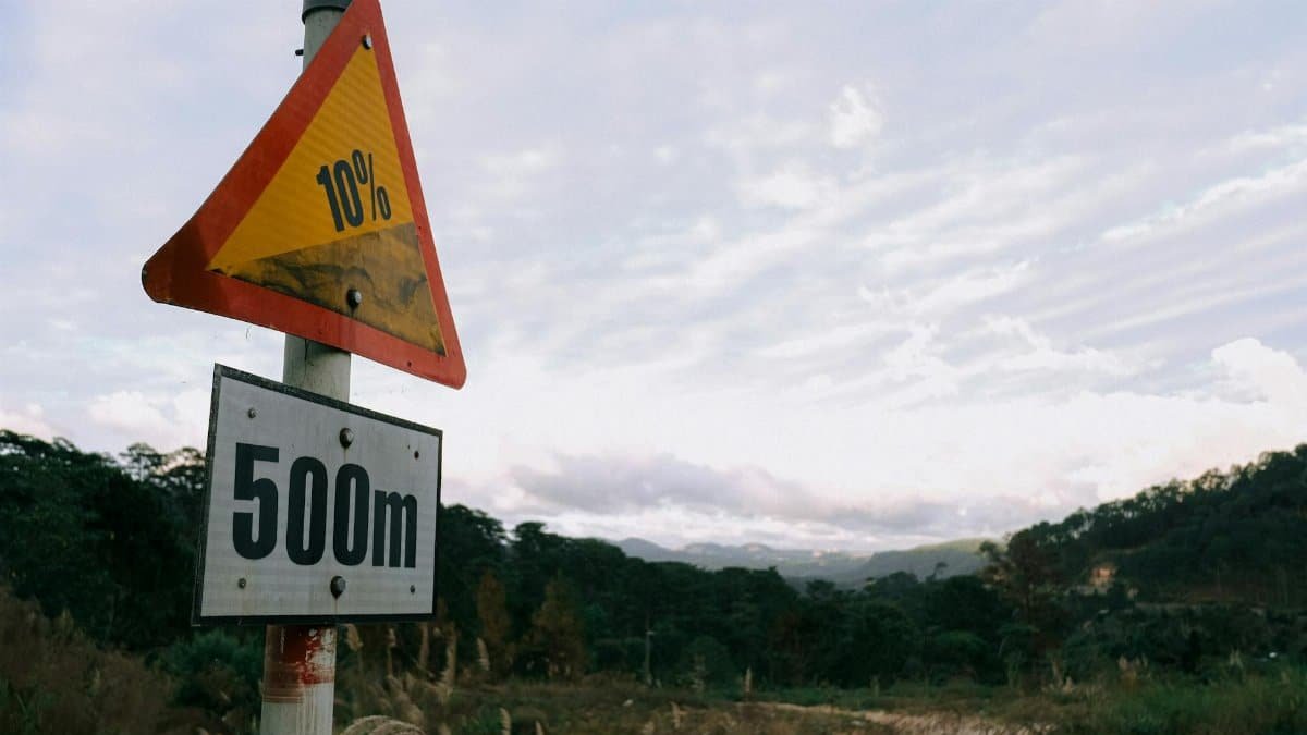 Road sign indicating a steep 10% descent over 500 meters in a hilly, scenic landscape.