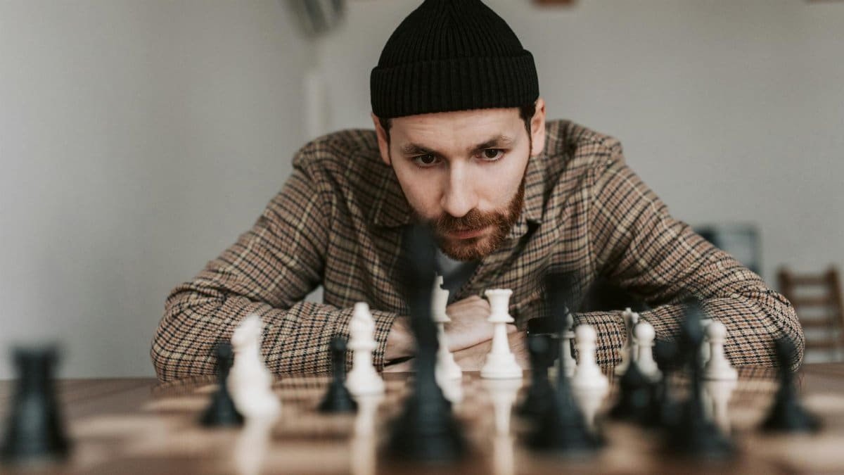 Focused man in beanie plays chess indoors, engaged in strategic thought.