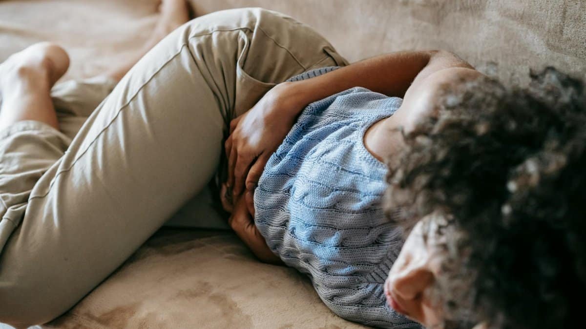 From above of crop anonymous African American female lying on couch and touching belly while having stomach ache
