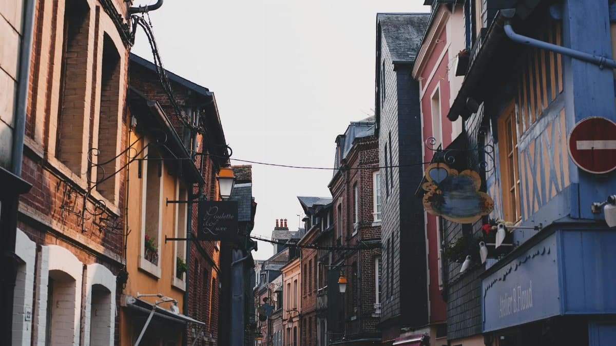 Narrow alley between typical buildings with colorful facade and brick walls located on street in town against cloudless sky in neighborhood