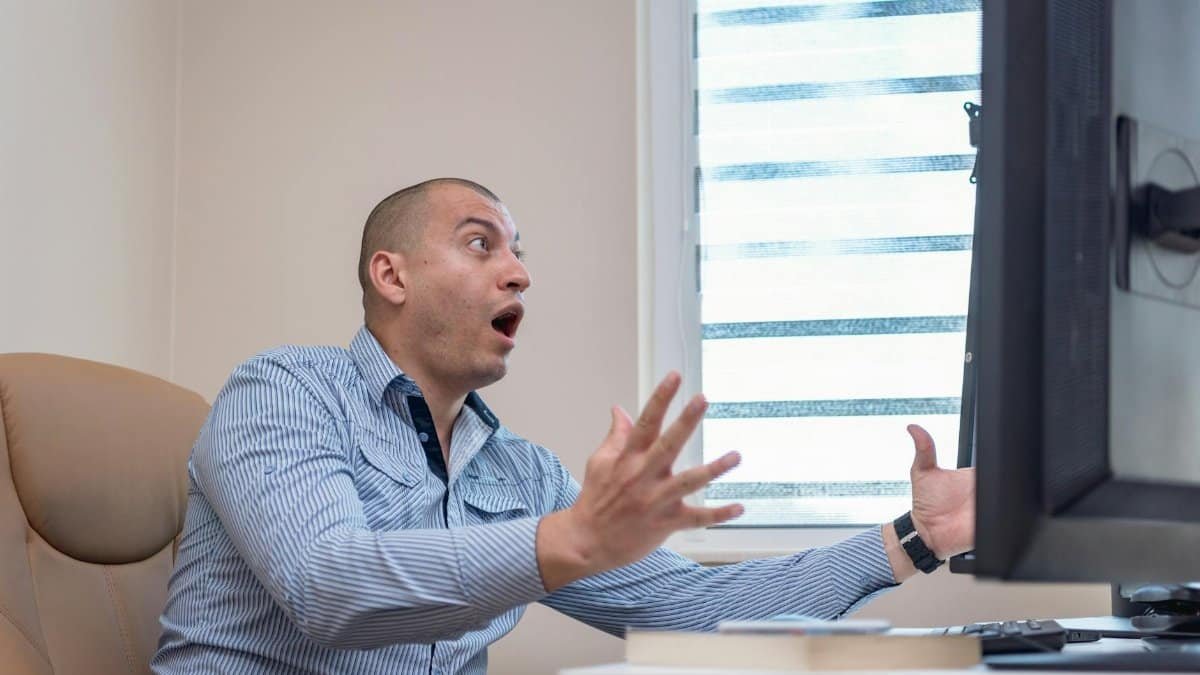 Man at desk shocked by computer screen in office setting.