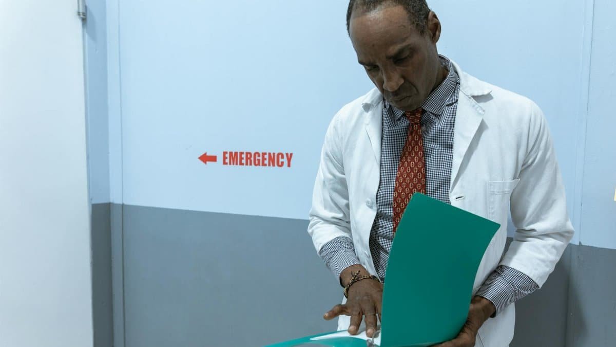 A doctor in a lab coat examines documents near the emergency room sign.