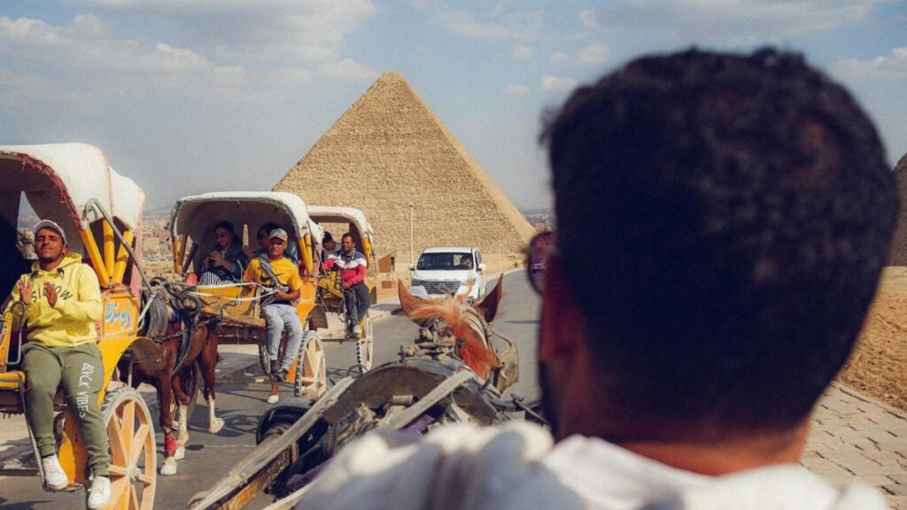 Tourists enjoy horse-drawn carriages near the iconic Giza pyramids on a sunny day.