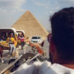 Tourists enjoy horse-drawn carriages near the iconic Giza pyramids on a sunny day.