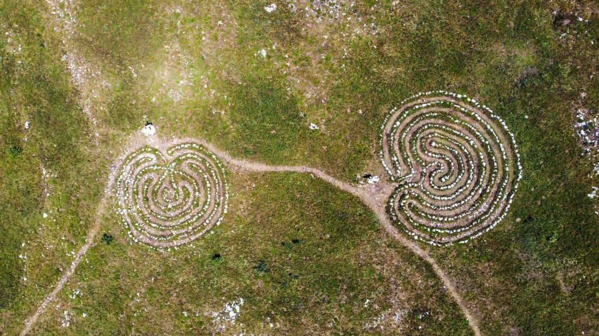 Two spiral stone labyrinths on a grassy field captured from above.