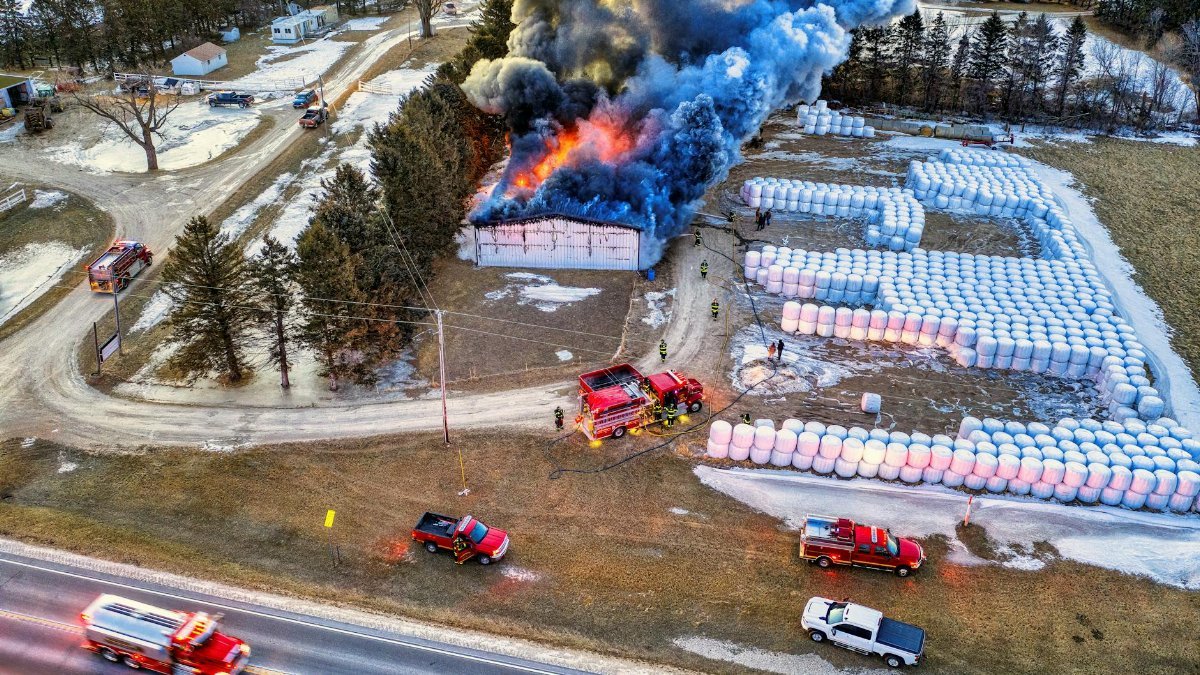 Intense aerial view of a blazing warehouse fire in Minnesota with fire trucks and smoke plumes.