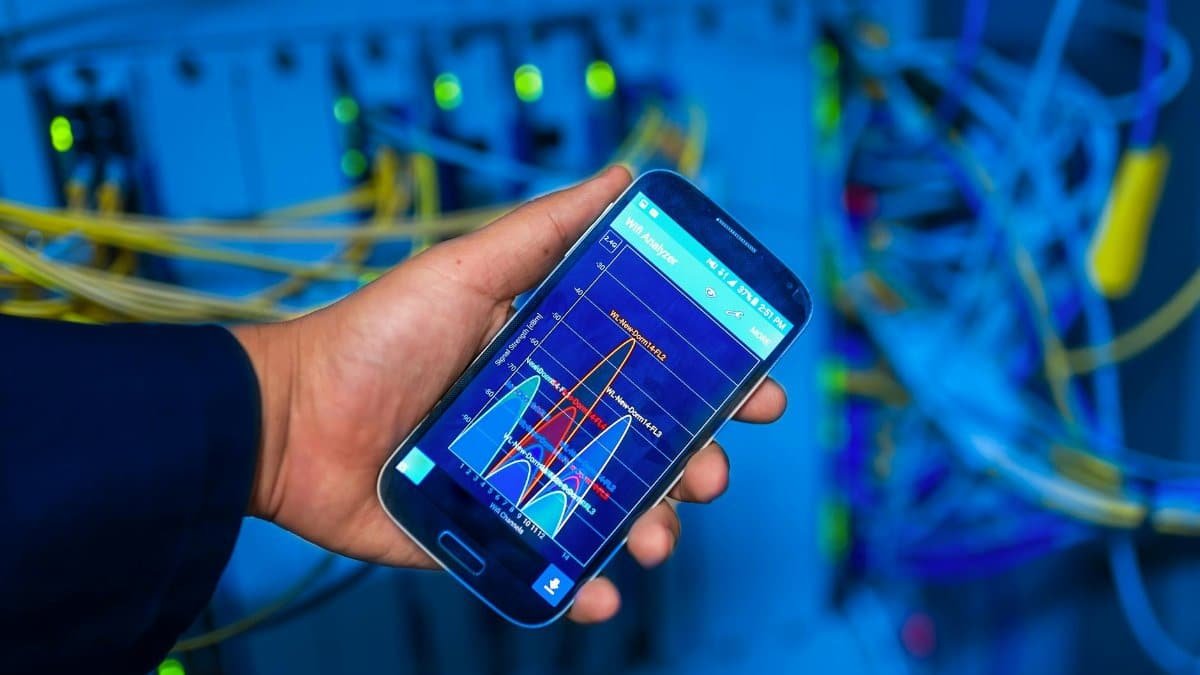 Hand holding smartphone displaying network analysis in high-tech server environment.