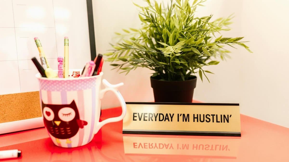 Bright desk setup featuring a motivational quote, potted plant, and cup of pens.