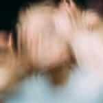 Through window blurred view of anonymous person imitating terrifying character while touching glass between blood fluid