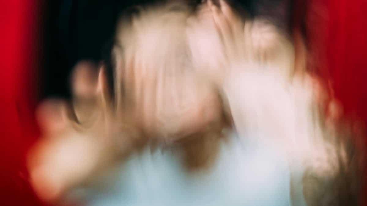 Through window blurred view of anonymous person imitating terrifying character while touching glass between blood fluid