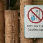 A sign prohibiting eating or drinking attached to wooden logs outdoors.
