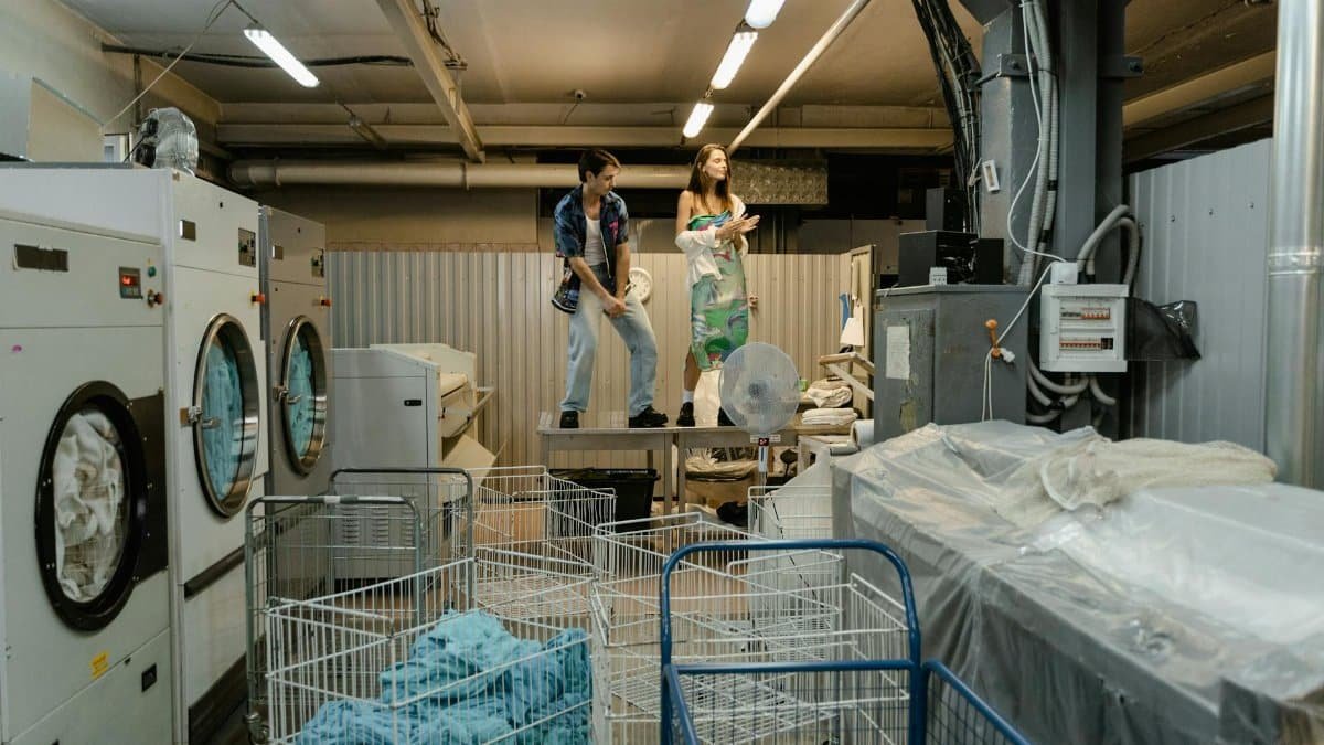 Two people take a break in a busy industrial laundry facility, surrounded by machines and laundry carts.