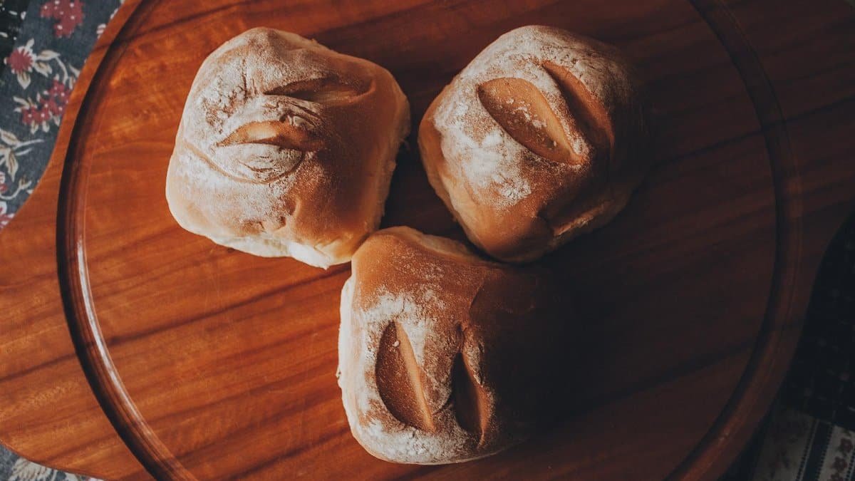 Top view of fresh artisan bread rolls on a wooden tray, perfect for food photography and culinary themes.