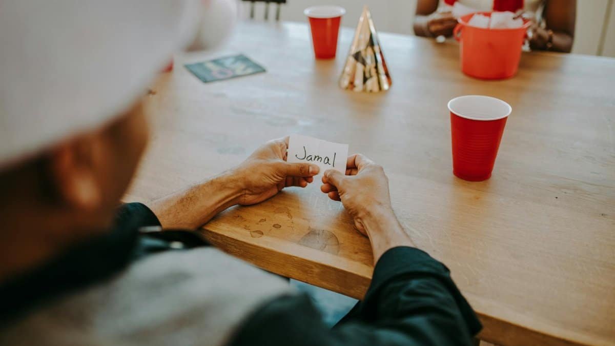 Casual indoor gathering scene with friends holding name card, red cups, and party hats on a wooden table.