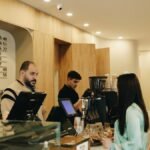 A modern café interior showing baristas preparing coffee and customers at the counter.