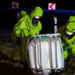 Two firefighters in hazmat suits managing a chemical spill by the roadside at night.
