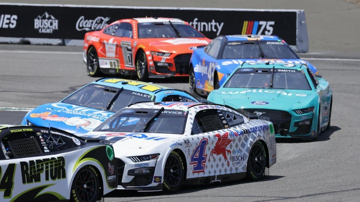 High-speed NASCAR cars race on a sunny day at a famous track, showcasing thrilling motorsport action.