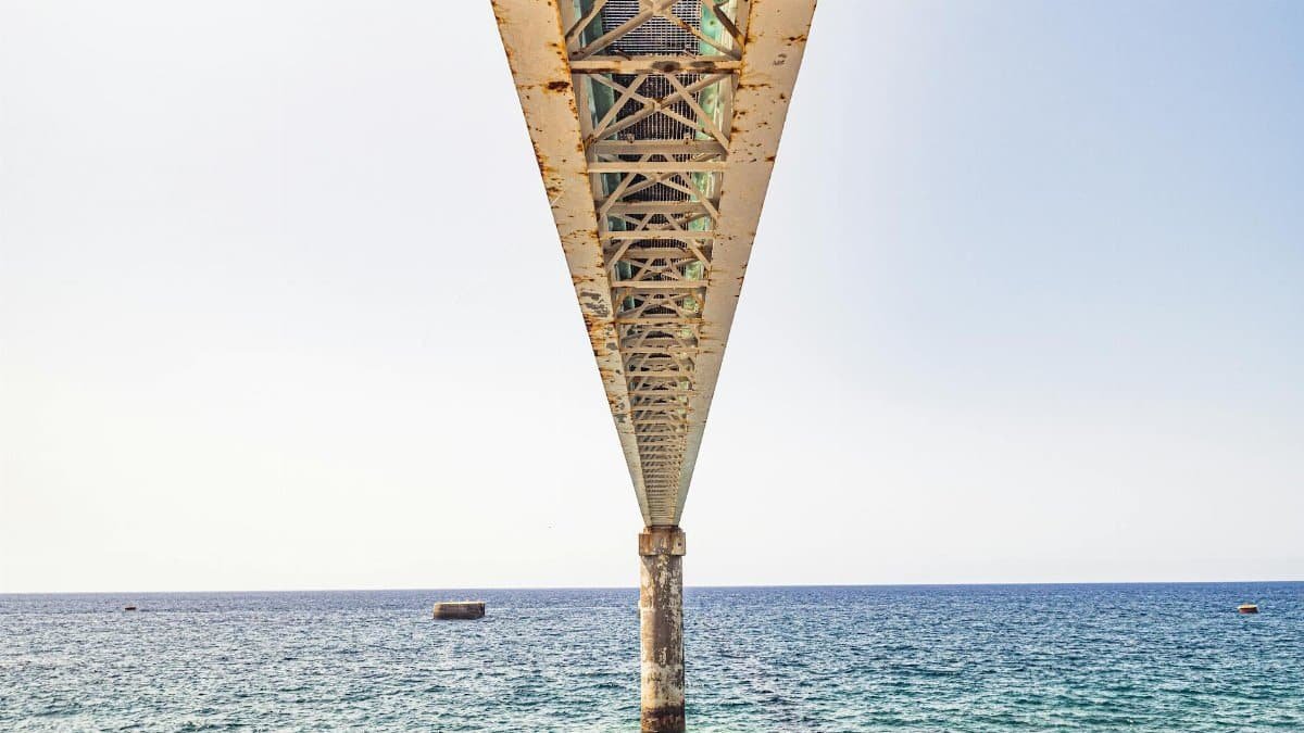 A rusty metal pier extends over the clear blue ocean in Madeira, Portugal.