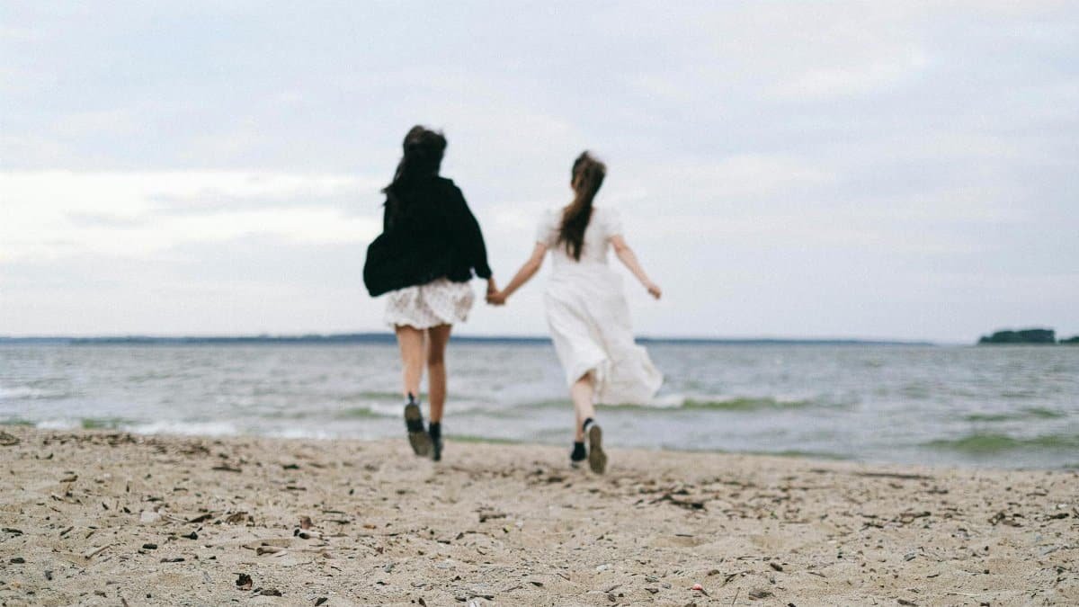 Two women run hand-in-hand on a sandy beach, capturing a moment of freedom and connection.