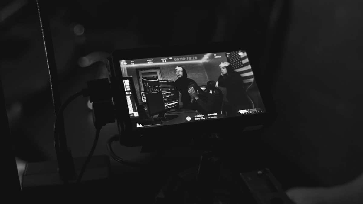 A monitor displaying a live stream of two individuals discussing content in a studio setting.