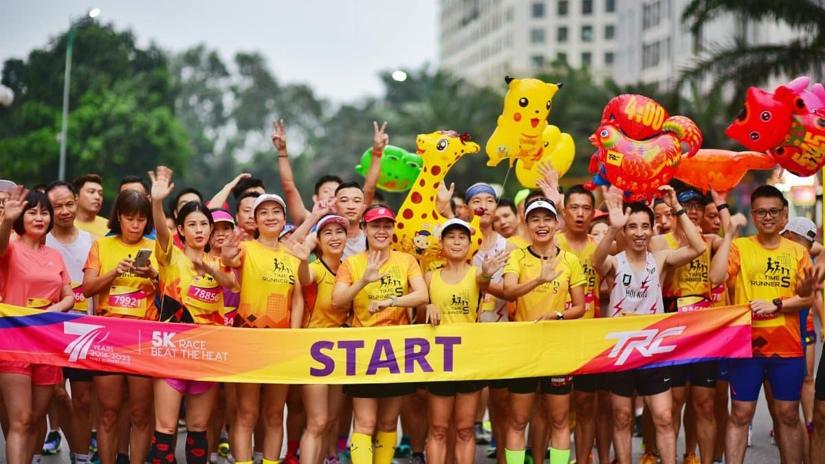 Cheerful runners at a 5K race start line holding colorful inflatable toys in a lively outdoor setting.
